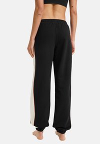 Schwarze Sweatpants mit einem weißen Seitenstreifen und orangefarbenen Abnähten, ausgestattet mit einem elastischen Bund und Bündchen an den Knöcheln, aus weichem Stoff gefertigt.