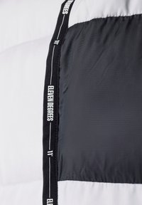 Chaqueta tipo plumón en blanco y negro. Presenta una textura suave, bloques de color horizontales y costuras con la marca a lo largo de la costura.