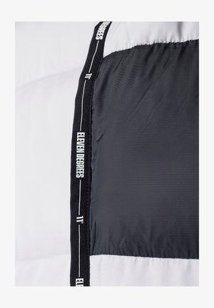 Chaqueta tipo plumón en blanco y negro. Presenta una textura suave, bloques de color horizontales y costuras con la marca a lo largo de la costura.