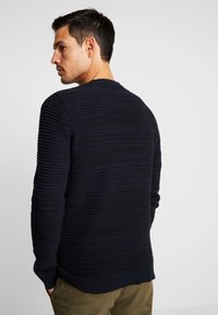Maglione a coste navy con strisce orizzontali testurizzate, collo rotondo e polsini a coste. Realizzato in un morbido tessuto a maglia. Vestibilità casual con una silhouette rilassata.