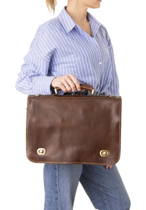 Sac à épaule en cuir marron avec quincaillerie dorée, de forme rectangulaire plate, avec des coutures visibles et une poignée en haut.