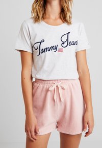 Šedé bavlněné tričko s logem „Tommy Jeans“ v námořnické modři. Světle růžové žebrované šortky s elastickým pasem a akcenty šňůrky.