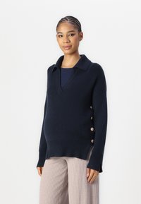 Navy knit sweater with a V-neck and collar, featuring side buttons. Chunky texture with ribbed hem and side slits for ease of movement.