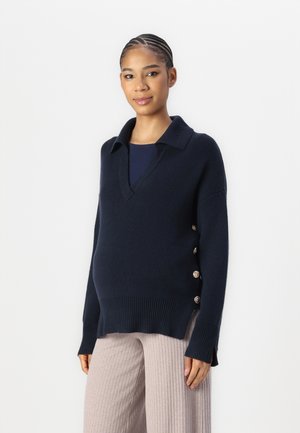 Navy knit sweater with a V-neck and collar, featuring side buttons. Chunky texture with ribbed hem and side slits for ease of movement.