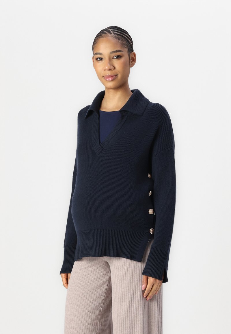 Navy knit sweater with a V-neck and collar, featuring side buttons. Chunky texture with ribbed hem and side slits for ease of movement.