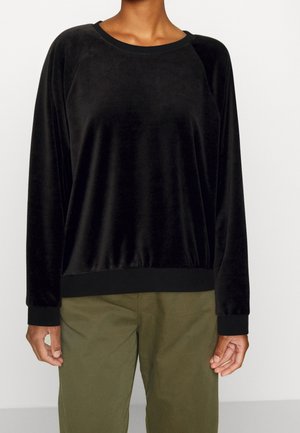 Pull-over en velours noir à manches longues avec encolure ronde, associé à un pantalon vert olive sur une personne debout.