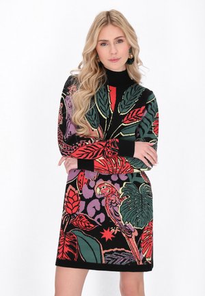 Rochie tricotată cu un bază neagră, decorată cu imprimeuri florale și cu papagali în nuanțe de roșu, verde și violet. Guler înalt și mâneci lungi, stil ajustat.