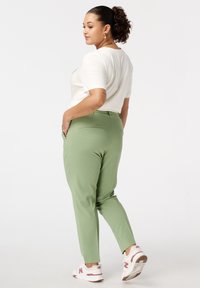 Lichtgroene, op maat gemaakte broeken met een gladde textuur, voorzien van achterzakken en voorzakken, gecombineerd met een eenvoudig wit t-shirt en witte sneakers.