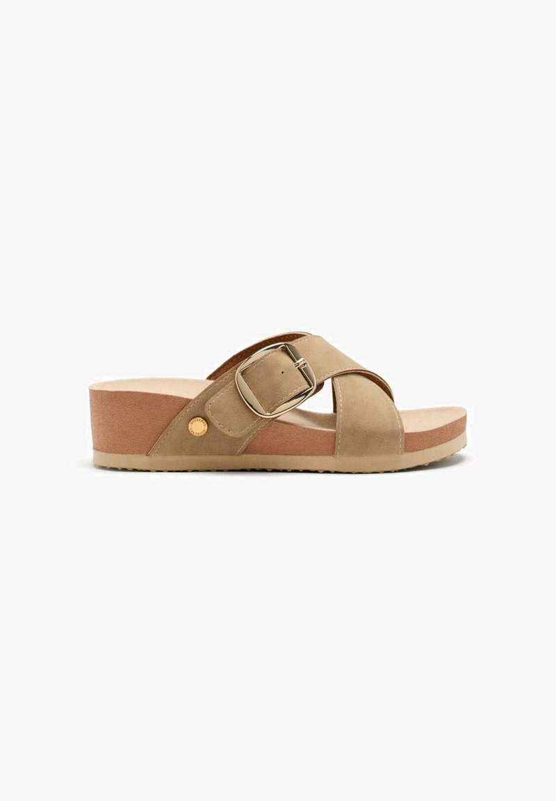 Sandal de plataforma beige con diseño de tiras cruzadas, hebilla metálica y parte superior suave y texturizada. Suela de color marrón claro con ligero agarre.