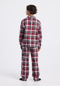 Red, green, and white plaid flannel pajamas with a button-up shirt and matching pants; loose fit; soft texture. Visible collar and cuffs.