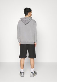 Grauer Kapuzenpullover mit lässigem Schnitt, kombiniert mit schwarzen Shorts. Zu den Merkmalen gehören gerippte Bündchen und eine strukturierte Kapuze. Lässiges Schuhwerk sichtbar.
