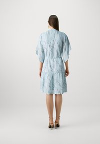 Robe bleu clair avec un motif ondulé, manches courtes évasées, taille cintrée et jupe à volants, associée à des escarpins à lanières.