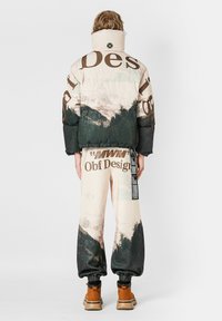 Chaqueta y pantalones acolchados en tonos pastel con estampado de montañas, letras grandes y puños elásticos; botas con suela de goma completan el conjunto.