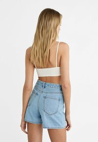 Top blanco ajustado tipo bralette con tirantes finos, combinado con pantalones cortos de mezclilla ligeros y de cintura alta en color azul claro. Los pantalones cortos cuentan con bolsillos traseros y un dobladillo deshilachado.
