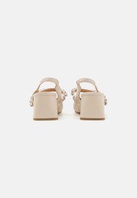 Sandali beige con tacco blocco, dalla texture liscia, con cinturino posteriore e decorazioni lungo i lati. Tacco chiuso e largo per una maggiore stabilità.
