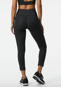 Leggings neri a vita alta realizzati in materiale elasticizzato, dotati di tasche laterali e un design snello e aderente che si stringe alla caviglia.