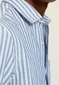 Lightweight, collared shirt with vertical blue and white stripes. Features button closure and fabric texture visible. Relaxed fit design.