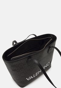 Svart Valentino toteväska med dubbla handtag, dragkedjestängning och mönster med logotyp på utsidan.