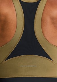 Top deportivo de color verde oliva y negro con paneles de malla y acentos cosidos; presenta la marca "SWISS ENGINEERING" en la parte baja de la espalda.