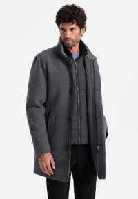 Abrigo de mezcla de lana gris con un cuello estructurado, botones y bolsillos laterales; cuenta con una capa interior aislante negra para mayor calidez.