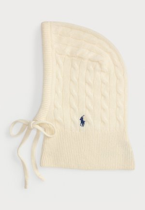 Bonnet crème en tricot à torsades avec un fond côtelé, arborant un logo bleu marine et des liens ajustables sur le côté. Texture douce.