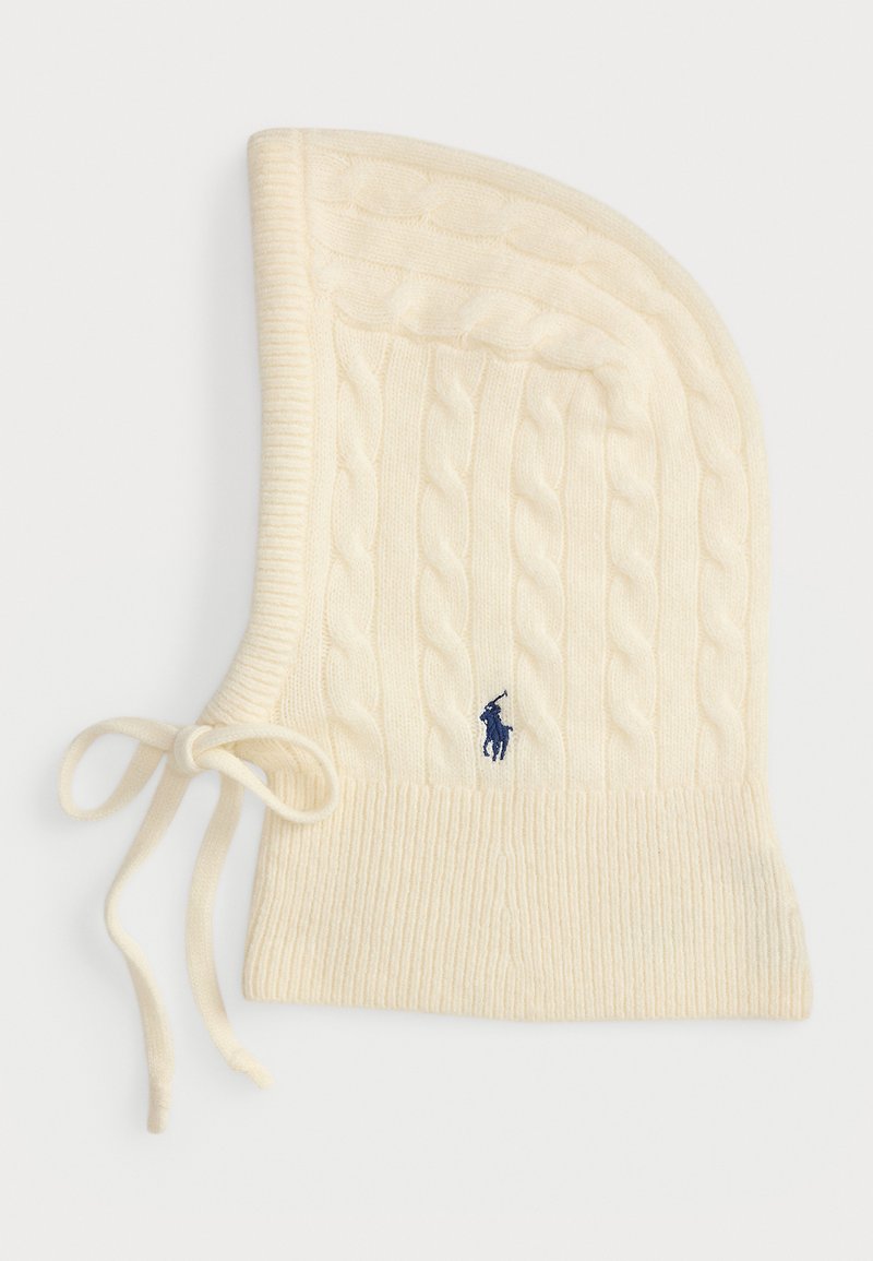 Gorro de malha creme em ponto trançado, com fundo canelado, apresentando um logotipo azul-marinho e laços ajustáveis de cada lado. Textura suave.