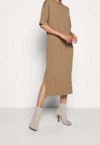 Vestido midi marrón de tela suave con un corte relajado, mangas cortas, aberturas laterales, y combinado con botas de tobillo beige con tacón de aguja.