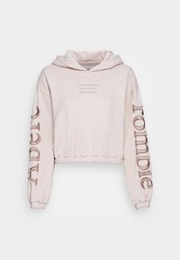 Světle růžová zkrácená mikina s kapucí na šňůrku, s vypouklým nápisem na hrudi a velkým designem na levém rukávu. Měkká látka.