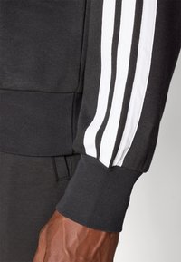 Sweatshirt preto com detalhes em faixa branca ao longo da manga. O tecido é texturizado com punhos canelados e um corte clássico.
