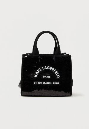Μαύρη γυναικεία τσάντα με δύο λαβές, καλυμμένη με παγιέτες, με λευκή επιγραφή "Karl Lagerfeld Paris 21 Rue St-Guillaume" στο μπροστινό μέρος.