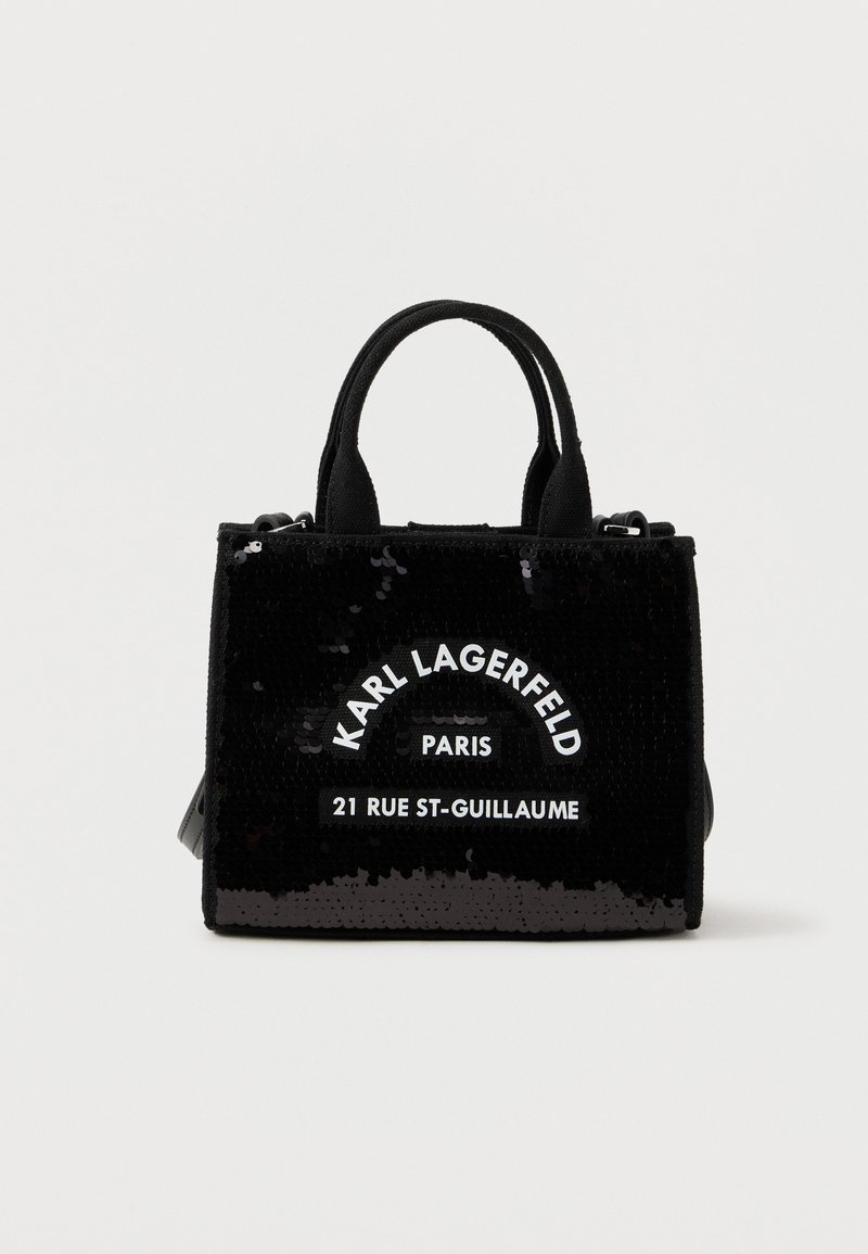 Μαύρη γυναικεία τσάντα με δύο λαβές, καλυμμένη με παγιέτες, με λευκή επιγραφή "Karl Lagerfeld Paris 21 Rue St-Guillaume" στο μπροστινό μέρος.