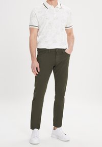Witte polo met bloemenpatroon, contrasterende kraag en manchetten; gecombineerd met olijfgroene slim-fit chinos; gedragen met witte sneakers.