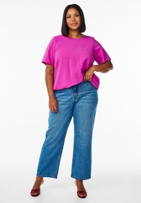 Top fucsia a maniche corte con colletto rotondo, abbinato a jeans blu chiaro a vita alta con gamba larga e sandali rossi con fasce.