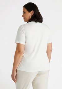Camiseta blanca de manga corta con escote redondeado; tela suave; diseño minimalista; textura lisa; combinada con pantalones de color claro.
