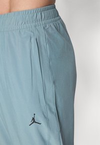 Light blue athletic pants with an elastic waistband, side pockets, and a black Jumpman logo on the thigh. Smooth fabric texture.