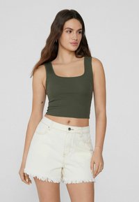 Top corto de color verde oscuro, con canalé y escote cuadrado, combinado con pantalones cortos de mezclilla blanca con bordes deshilachados. Diseño simple, forma ajustada.