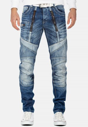 Denim-Jeans in einer verblassten blauen Farbe, mit Reißverschluss-Taschen, schrägen Nähten und unterschiedlichen Texturen. Akzentuiert mit einem weißen Gürtel.