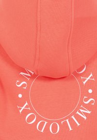 Haut à capuche corail au toucher doux, arborant un grand logo circulaire blanc dans le dos. Comprend une capuche avec cordon de serrage et des poignets côtelés.