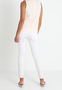 Top sin mangas de color beige claro con una textura suave, combinado con jeans blancos ajustados y sandalias de tacón azul claro, visto desde atrás.