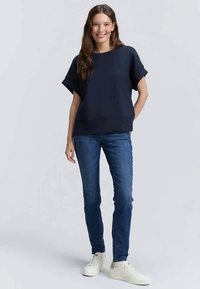 Tengerészeti rövid ujjú pulóver, amely laza fazonú, vékony kék farmernadrággal és fehér sportcipővel párosítva. Sima textúra és bordázott alsó szegély részletezés.