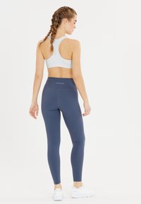 Sport-BH i vitt med racerback-design, tillsammans med åtsittande marinblå tights. Båda är tillverkade av stretchigt tyg med en mjuk textur.