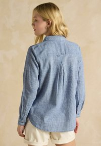 Lichtblauw geruit overhemd met lange mouwen, knoopmanchetten en een rugplooi. De stof lijkt zacht met een gewoven patroon.