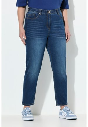 Jeans denim w ciemnym odcieniu z wysokim stanem, z zapięciem na guzik, przednimi kieszeniami i prostymi nogawkami. Noszone z jasnoniebieskimi trampkami.