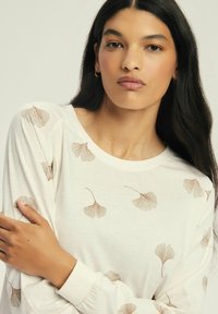 Long-sleeve cream top with scattered brown ginkgo leaf prints; soft fabric, round neckline, and fitted sleeves. Simple, elegant design.