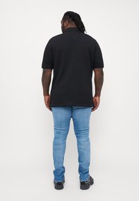 Sort polo shirt med korte ærmer, ensfarvet, parret med lyseblå jeans og sorte sko, set fra ryggen.