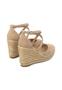 Des talons compensés en suède beige présentent une semelle épaisse en jute tissé et des brides de cheville entrecroisées, avec un bout rond et une texture lisse.