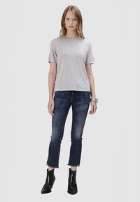 T-shirt gris à manches courtes en tissu doux, associée à un jean court bleu foncé avec des ourlets effilochés et des bottines noires.