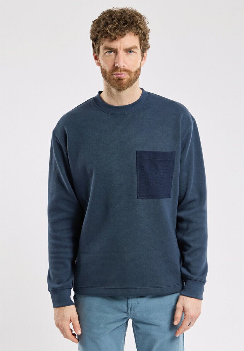 Sweatshirt bleu marine à manches longues, col rond et poche texturée sur la poitrine gauche. Tissu doux avec une coupe décontractée.