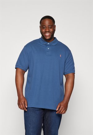 Polo de manga corta en algodón azul oscuro, con una abertura de tres botones, logo bordado y ajuste relajado. Combinado con jeans azules.