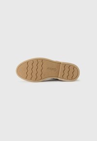 Rubber sole with textured grip patterns and visible grooves. The color is tan with a slight sheen. Logo embossed on the midsole.